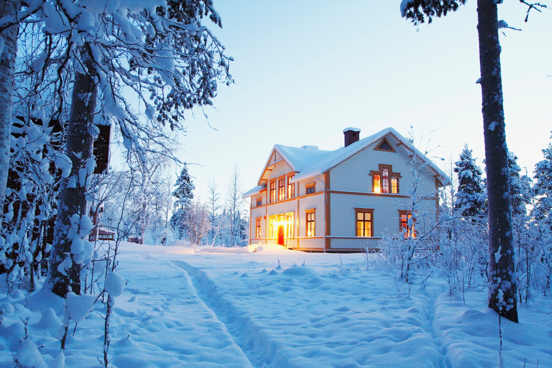 Ett snötäckt hus i en vinterlandskap med varmt ljus som lyser genom fönstren, vilket ger en känsla av komfort. Mitsubishi Electrics värmesystem hjälper till att upprätthålla en jämn och behaglig inomhustemperatur även under kalla vinterförhållanden.